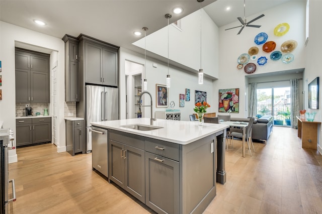 kitchen with sink, light wood-type flooring, hanging light fixtures, a high ceiling, and a kitchen island with sink