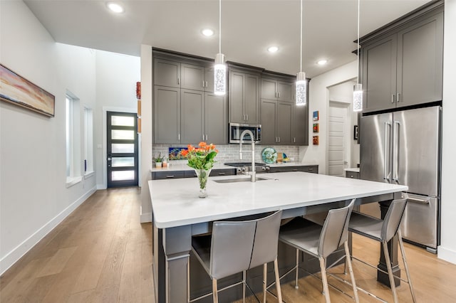 kitchen with a kitchen bar, light hardwood / wood-style floors, stainless steel appliances, decorative light fixtures, and a kitchen island with sink