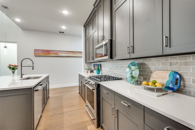 kitchen featuring gray cabinetry, sink, backsplash, light hardwood / wood-style floors, and stainless steel appliances