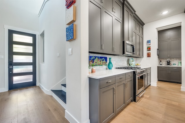 kitchen with gray cabinetry, appliances with stainless steel finishes, light wood-type flooring, and decorative backsplash