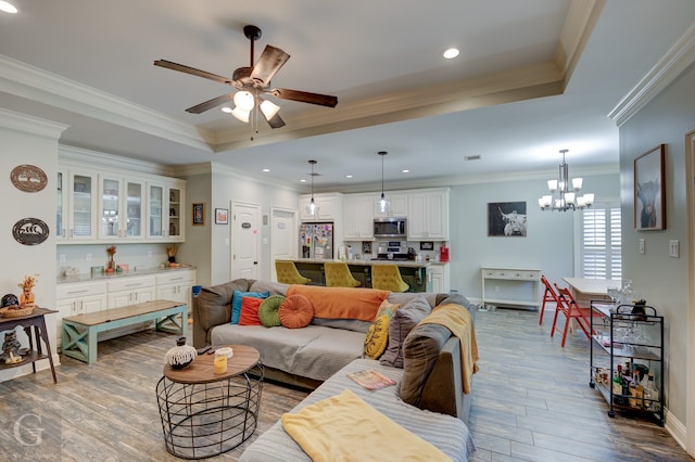 living room with crown molding, hardwood / wood-style floors, a tray ceiling, and ceiling fan with notable chandelier