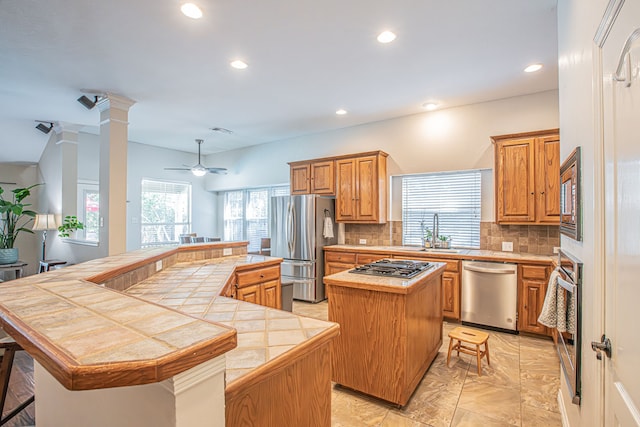 kitchen featuring tasteful backsplash, a kitchen island, tile countertops, ceiling fan, and stainless steel appliances