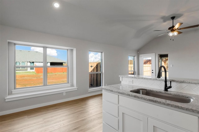 kitchen with light stone countertops, white cabinetry, lofted ceiling, and sink