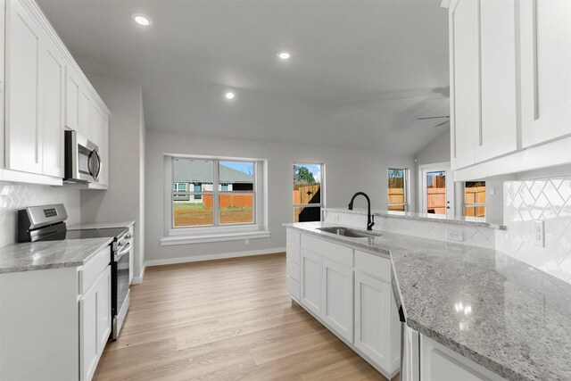 kitchen with light stone countertops, appliances with stainless steel finishes, vaulted ceiling, sink, and white cabinets