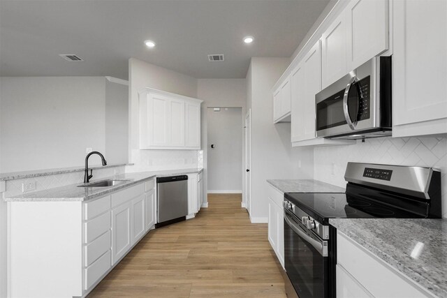 kitchen featuring white cabinets, appliances with stainless steel finishes, light stone countertops, and sink