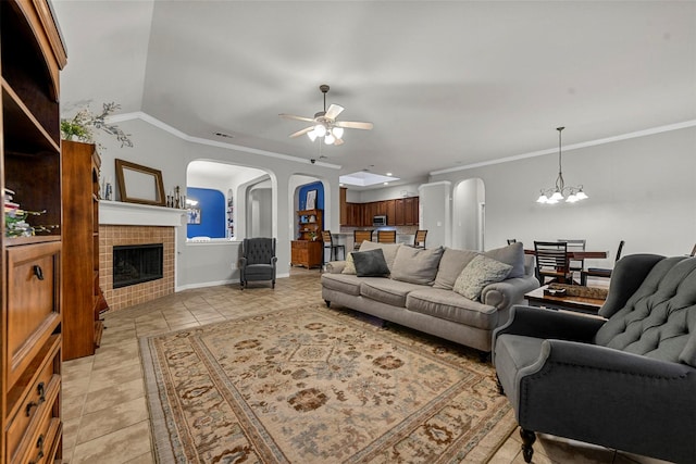 tiled living room with ceiling fan with notable chandelier, a tiled fireplace, ornamental molding, and lofted ceiling