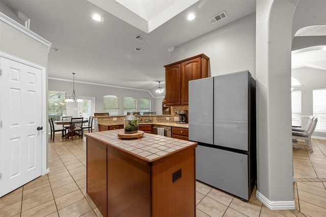 kitchen featuring stainless steel appliances, tile countertops, light tile patterned flooring, kitchen peninsula, and a kitchen island