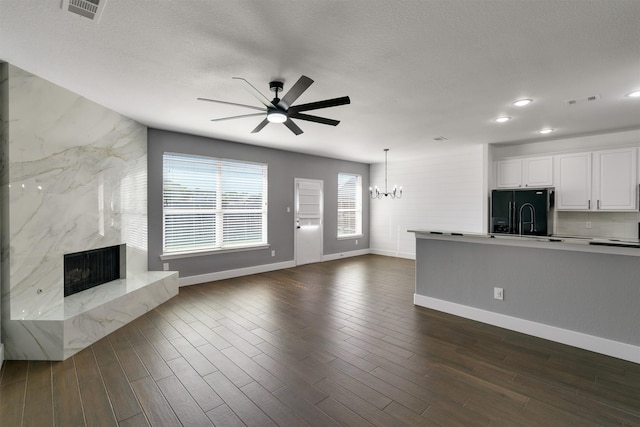 unfurnished living room with dark hardwood / wood-style floors, a premium fireplace, sink, a textured ceiling, and ceiling fan with notable chandelier