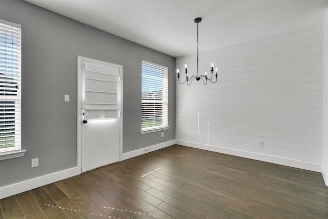 unfurnished dining area with dark wood-type flooring and an inviting chandelier