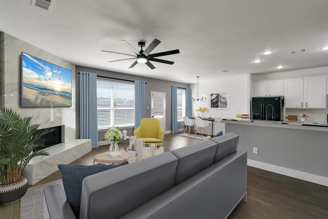 living room featuring a high end fireplace, sink, a textured ceiling, ceiling fan with notable chandelier, and dark hardwood / wood-style flooring