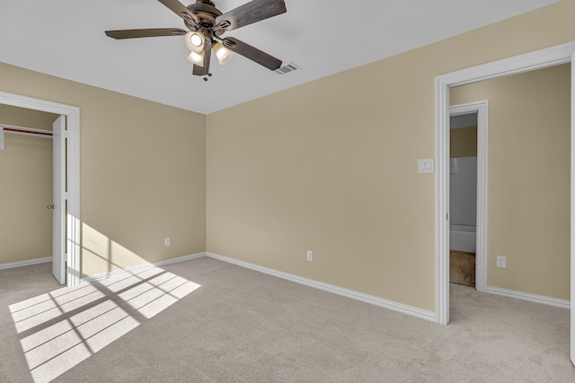 unfurnished bedroom featuring light carpet, a closet, a walk in closet, and ceiling fan