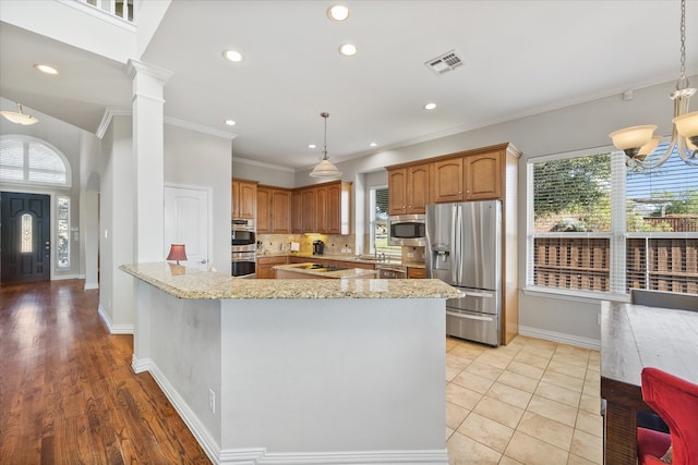 kitchen featuring light stone counters, an inviting chandelier, decorative light fixtures, appliances with stainless steel finishes, and decorative columns