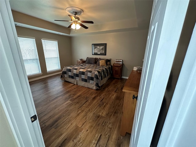 bedroom with a raised ceiling, ceiling fan, and dark wood-type flooring