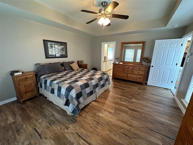 bedroom with dark hardwood / wood-style floors, ceiling fan, a raised ceiling, and connected bathroom