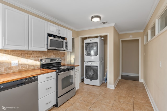 kitchen featuring appliances with stainless steel finishes, backsplash, butcher block counters, white cabinetry, and stacked washing maching and dryer