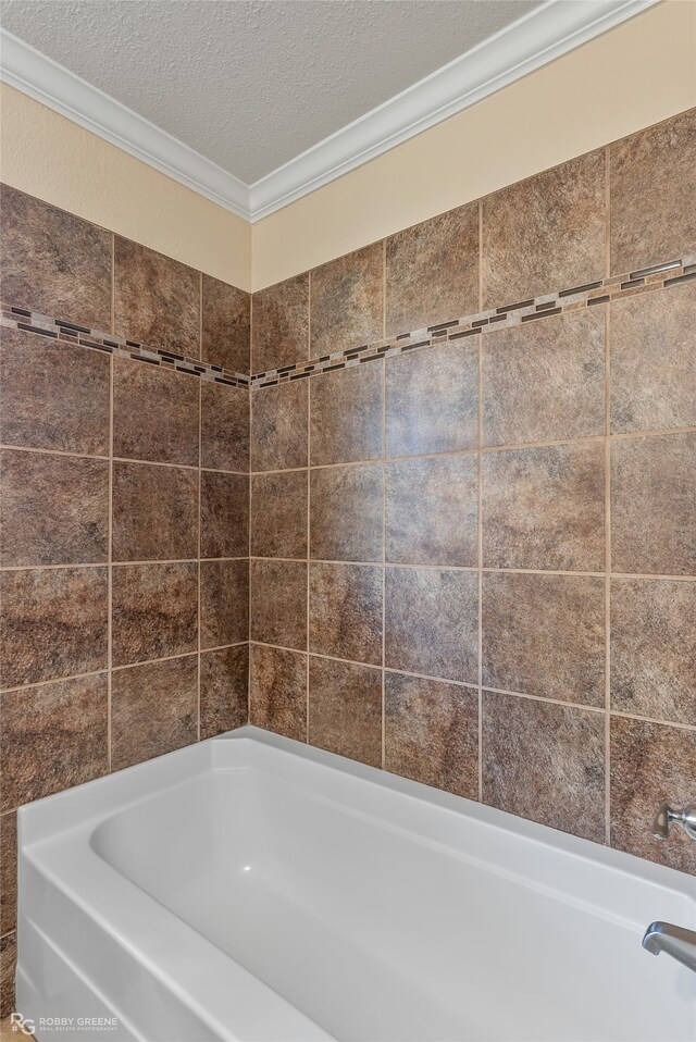 bathroom featuring a textured ceiling, ornamental molding, and a bathing tub