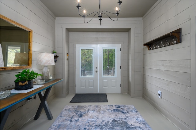 doorway with french doors, a notable chandelier, and wooden walls