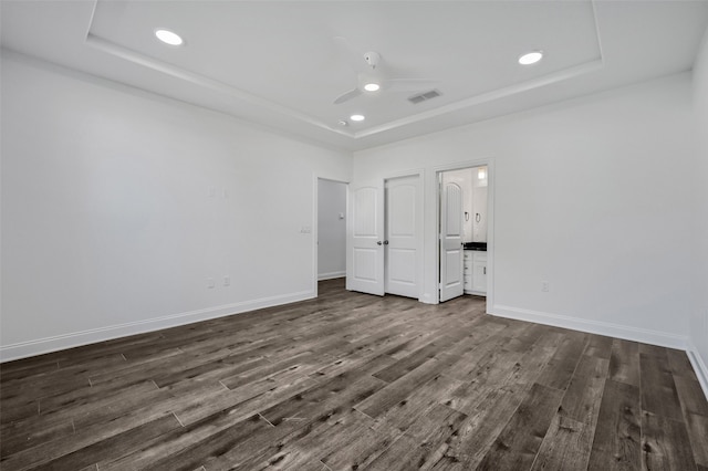 unfurnished bedroom featuring connected bathroom, a tray ceiling, dark wood-type flooring, and ceiling fan