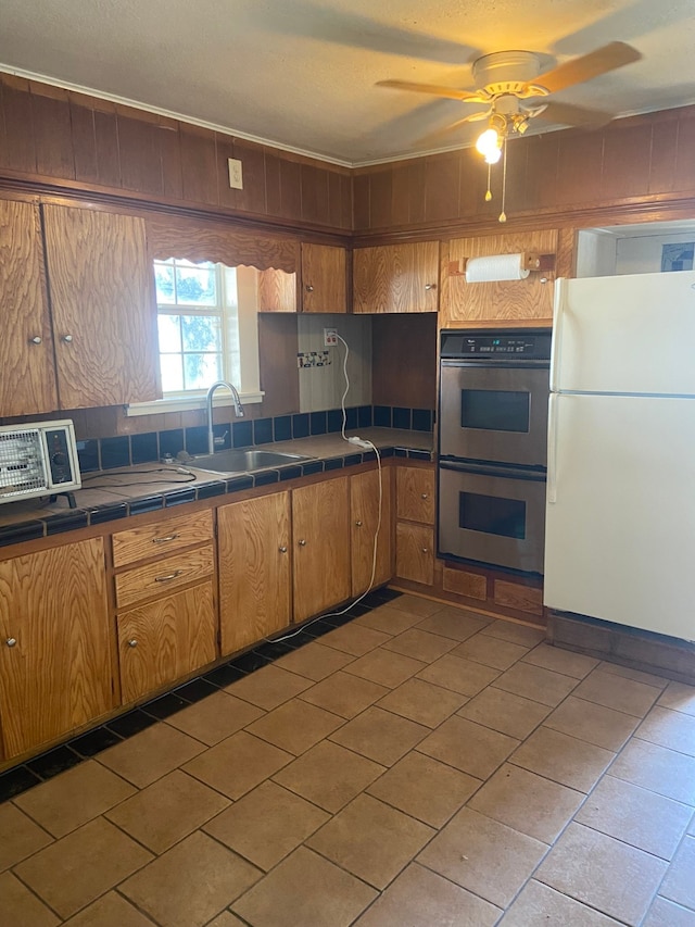 kitchen featuring double oven, tile countertops, sink, white refrigerator, and ceiling fan