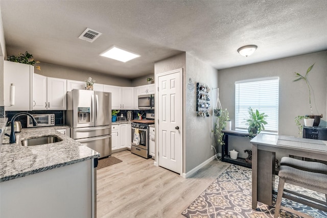 kitchen with sink, light stone counters, light hardwood / wood-style flooring, white cabinets, and appliances with stainless steel finishes