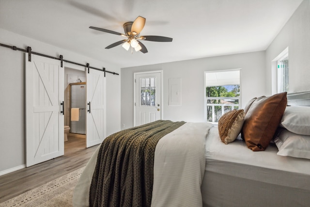 bedroom featuring light hardwood / wood-style floors, a barn door, ceiling fan, and ensuite bath