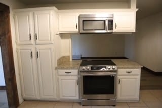 kitchen featuring light stone countertops, white cabinets, light tile patterned flooring, and appliances with stainless steel finishes