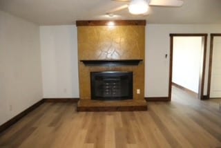 unfurnished living room featuring hardwood / wood-style floors, ceiling fan, and a large fireplace