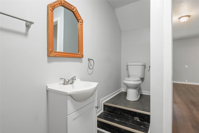 bathroom with vanity, hardwood / wood-style floors, vaulted ceiling, and toilet