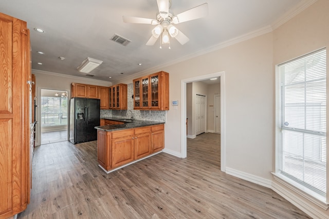 kitchen with tasteful backsplash, dark stone counters, crown molding, black fridge, and light hardwood / wood-style flooring