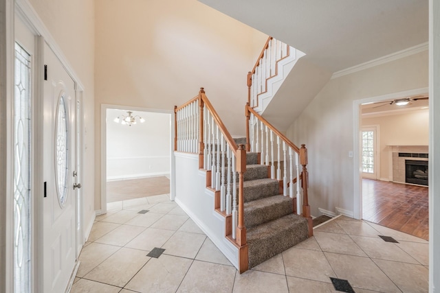 foyer entrance featuring a towering ceiling, ceiling fan with notable chandelier, a tiled fireplace, light tile patterned floors, and crown molding