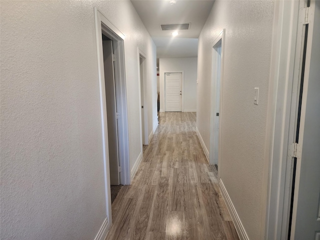 corridor with baseboards, a textured wall, visible vents, and wood finished floors