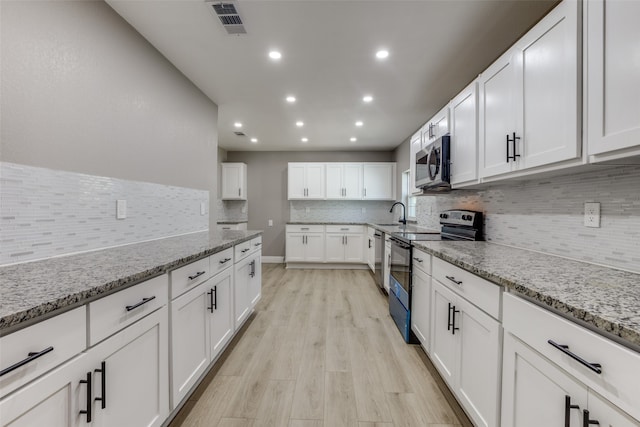 kitchen with appliances with stainless steel finishes, light hardwood / wood-style flooring, white cabinetry, and light stone countertops