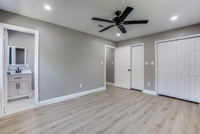 unfurnished bedroom featuring ceiling fan, multiple closets, ensuite bathroom, light hardwood / wood-style floors, and sink