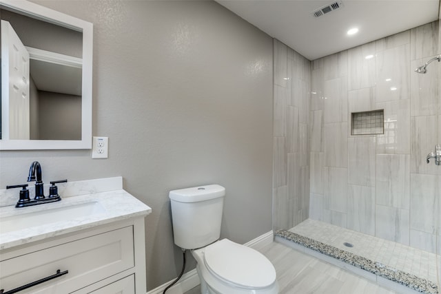 bathroom featuring vanity, a tile shower, and toilet