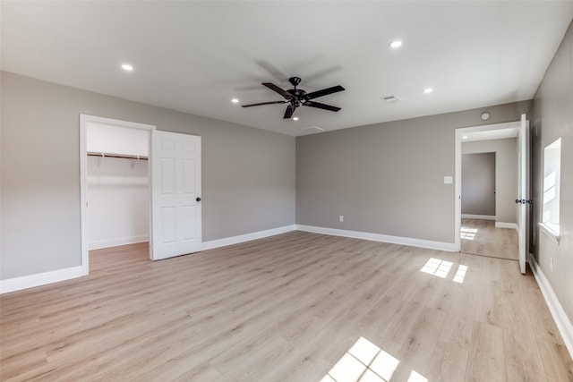 unfurnished bedroom featuring a walk in closet, a closet, light wood-type flooring, and ceiling fan