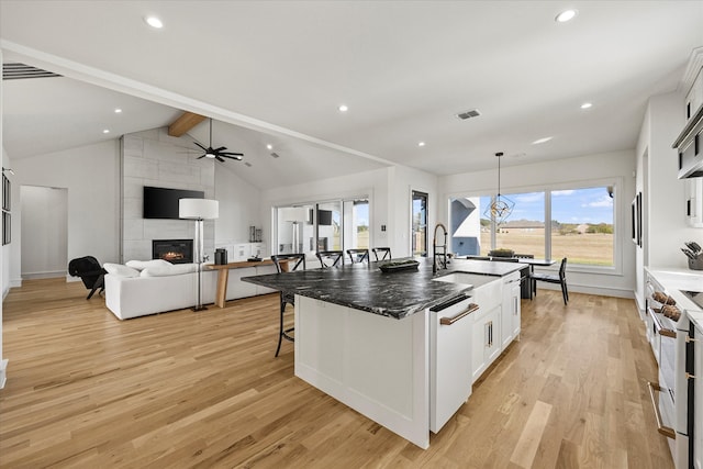 kitchen featuring stainless steel stove, white cabinets, a kitchen breakfast bar, white dishwasher, and a center island with sink