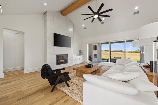 living room featuring high vaulted ceiling, a fireplace, beamed ceiling, ceiling fan, and light wood-type flooring