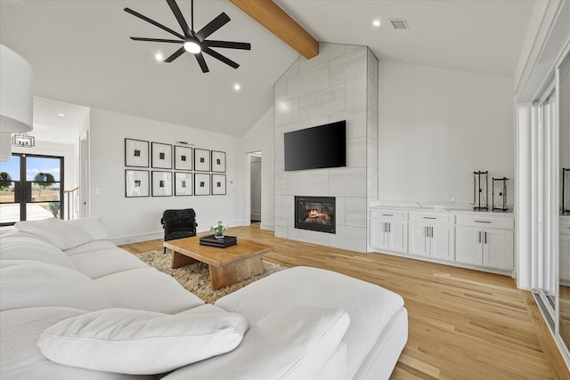 living room featuring beamed ceiling, high vaulted ceiling, a tiled fireplace, and light hardwood / wood-style floors