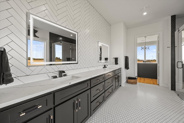 bathroom with baseboards, a shower with shower door, double vanity, and a sink