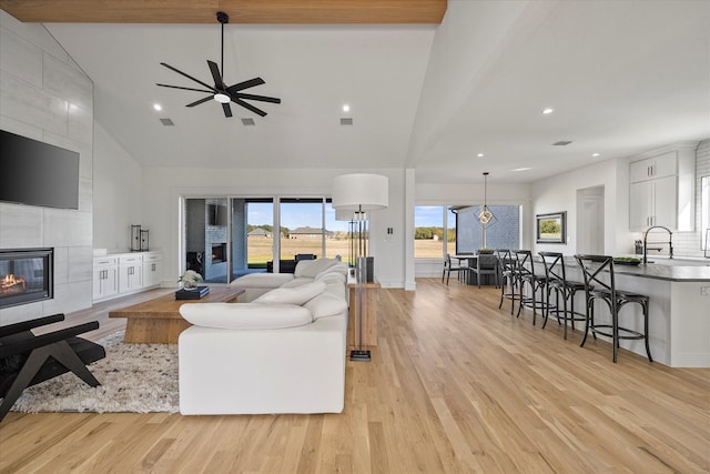 living room with sink, a tile fireplace, ceiling fan, high vaulted ceiling, and light hardwood / wood-style floors