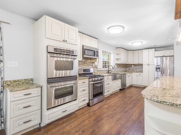 kitchen with light stone countertops, appliances with stainless steel finishes, dark hardwood / wood-style floors, and white cabinetry