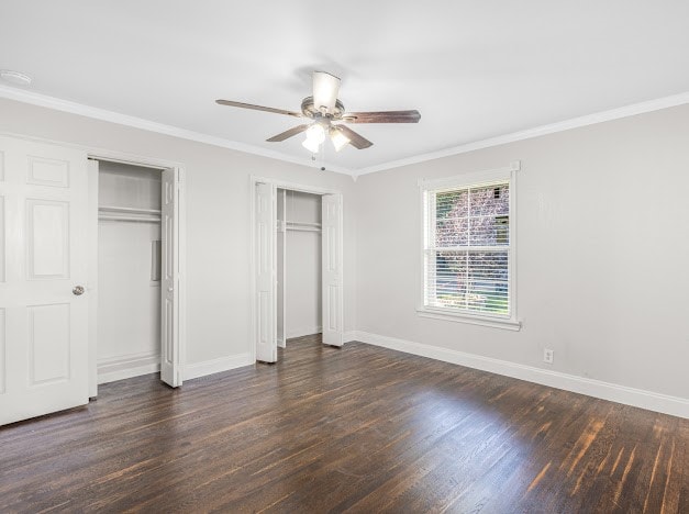 unfurnished bedroom with dark hardwood / wood-style flooring, crown molding, two closets, and ceiling fan