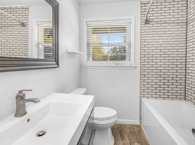 full bathroom featuring toilet, tiled shower / bath, wood-type flooring, and plenty of natural light