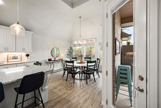 dining area with light wood-type flooring, vaulted ceiling, and a chandelier