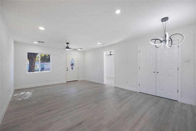 unfurnished living room featuring ceiling fan with notable chandelier and light wood-type flooring