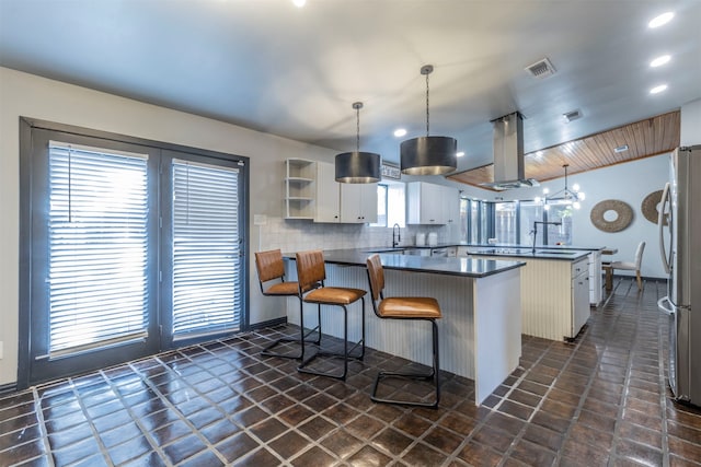 kitchen with island exhaust hood, kitchen peninsula, backsplash, decorative light fixtures, and white cabinetry