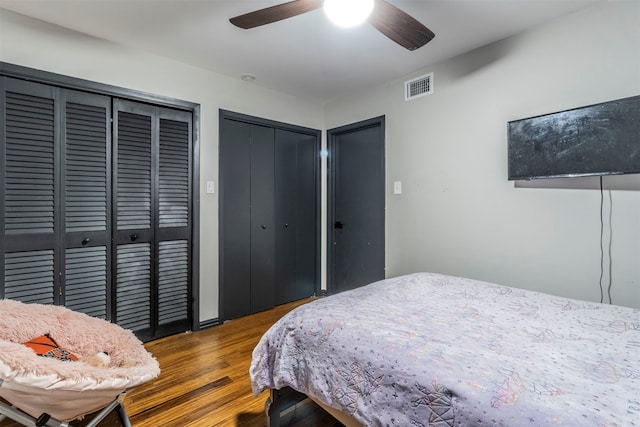 bedroom featuring dark wood-type flooring, ceiling fan, and multiple closets