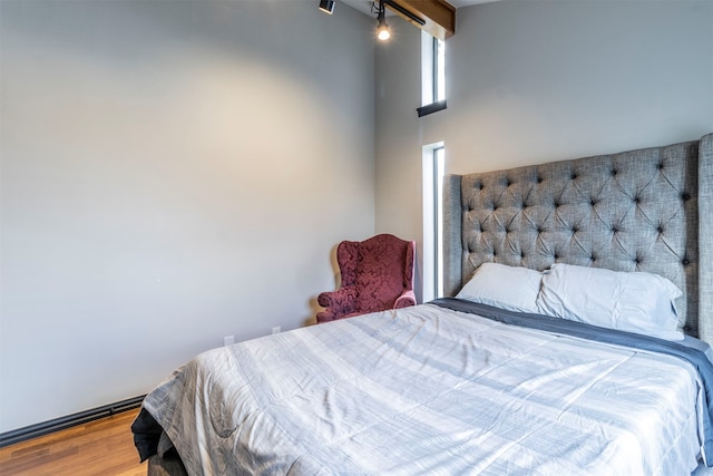 bedroom featuring a towering ceiling, beamed ceiling, and hardwood / wood-style floors