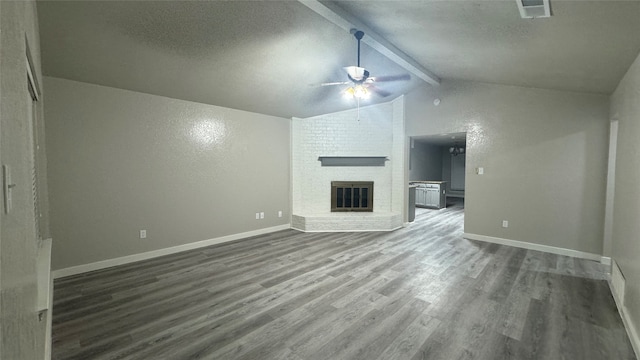 unfurnished living room with hardwood / wood-style floors, ceiling fan, a textured ceiling, a brick fireplace, and lofted ceiling with beams