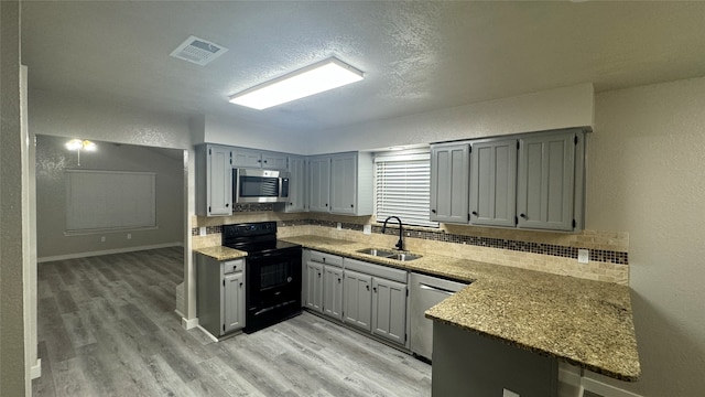 kitchen with light stone countertops, sink, light wood-type flooring, kitchen peninsula, and stainless steel appliances